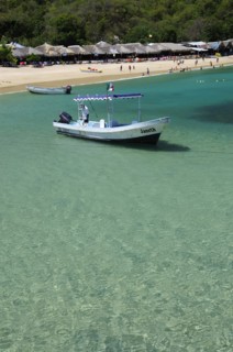Mexico, Oaxaca, Huatulco, Playa La Entrega Tour boat moored in clear shallow water in foreground of