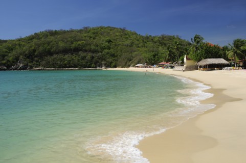Mexico, Oaxaca, Huatulco, Sandy beach at Bahia Santa Cruz lined by restaurants and other buildings