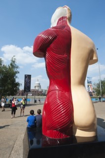 Two children pose for a photograph in front of Damian Hirst's sculpture, 'Hymn', the South Bank, Londonn