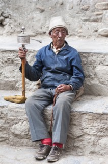 Nepal, Upper Mustang, Lo Manthang, Elderly man praying with prayer wheel in the square near the
