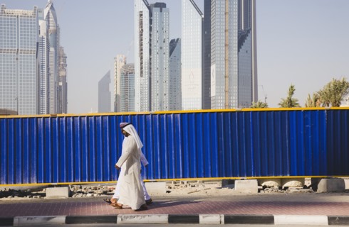 UAE, Dubai, Arab men dressed in tradityional Dishdasha walking past construction site with Sheikh
