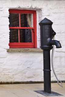 Ireland, North, Derry, Craft Village, Old water pump with small red window in background. 
Photo