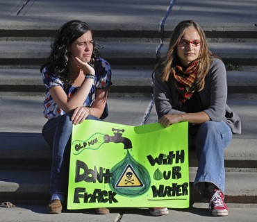 Canada, Alberta, Lethbridge, Two local women atsitting on stone steps at an anti-fracking demonstration holding a green protest sign. Oldman River  which runs through Lethbridge  is the source of the ...